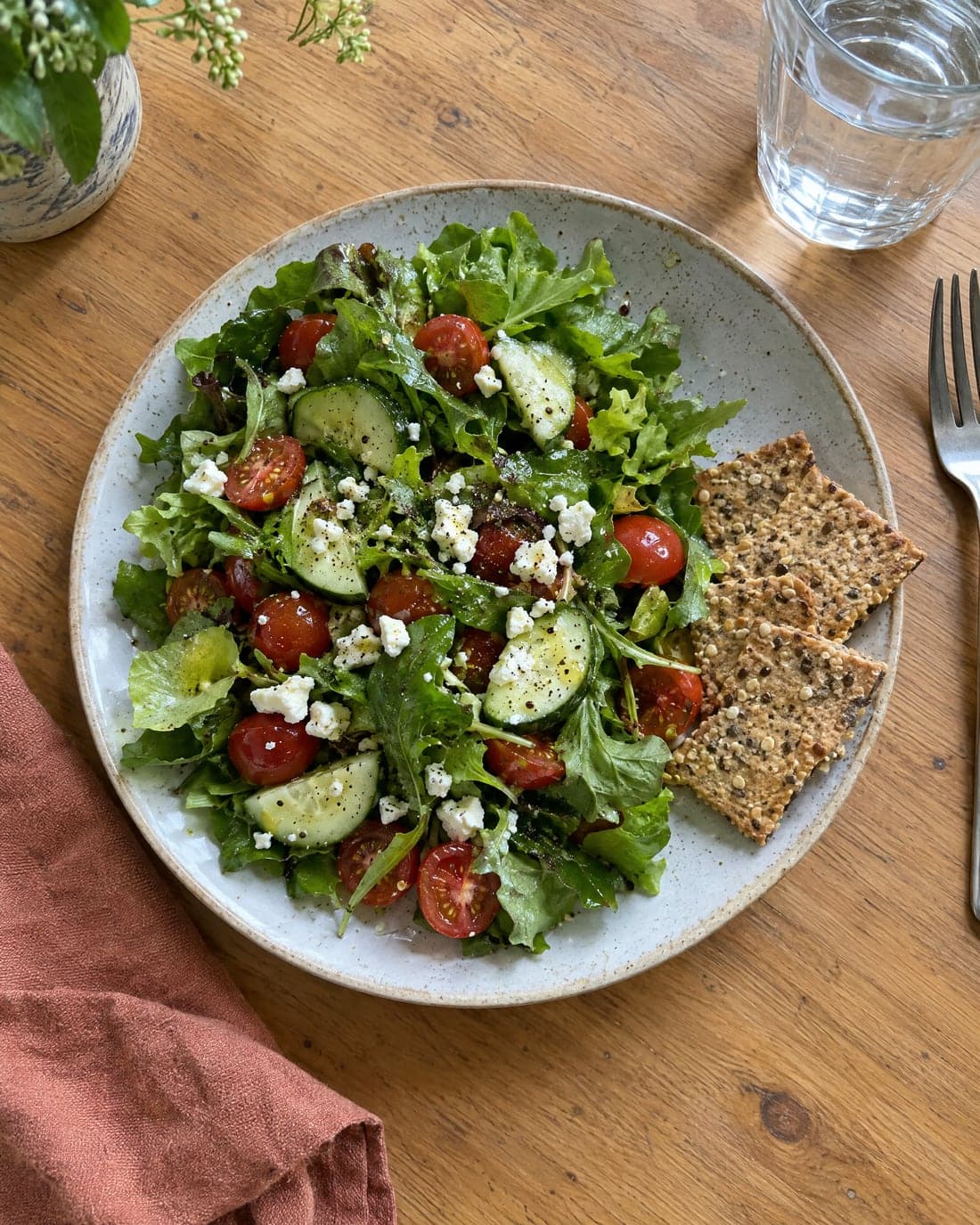 A salad with tomatoes, cucumber, feta and crackers on a plate.